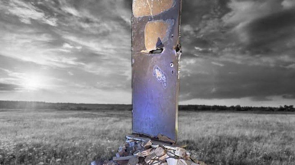 Field with single door standing on a pile of rubble. It is lit from below with puple light.