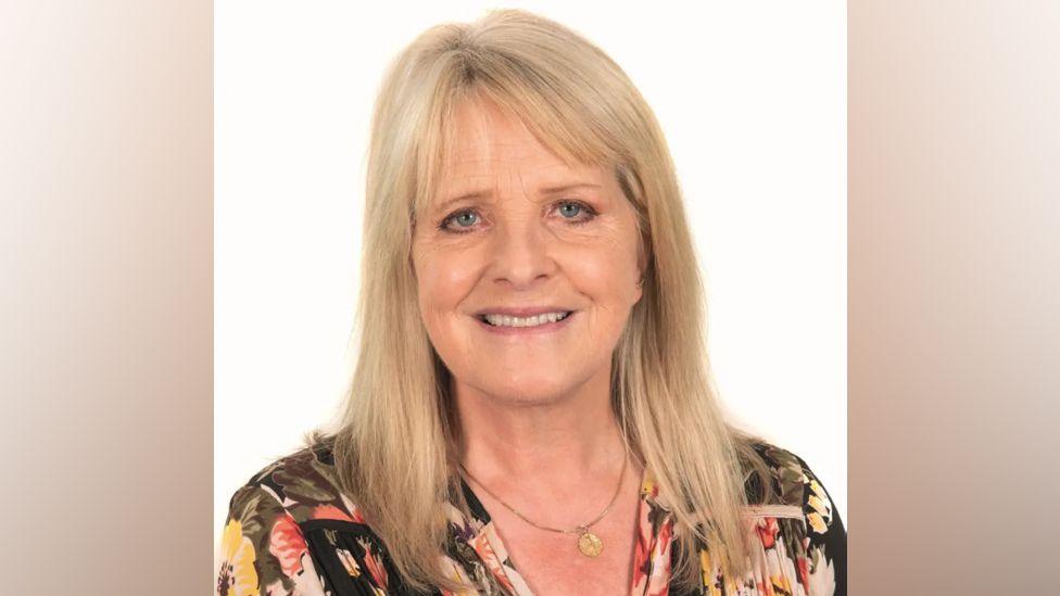 A picture of Councillor Angela Macpherson who has blonde hair and is wearing a black floral blouse.