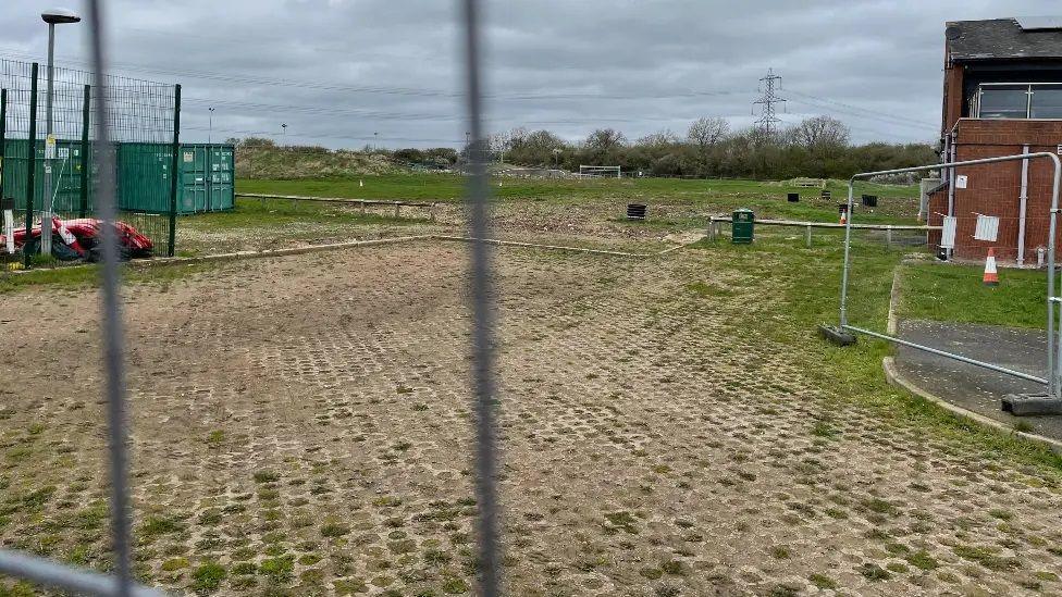 A patch of empty land with safety matting and grass with fencing around it where part of a BMX track was previously accessed