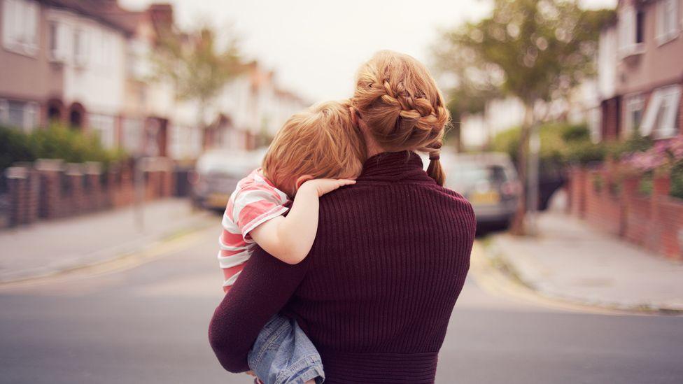 Rear view of a woman carrying a child in a street. Their faces are hidden.