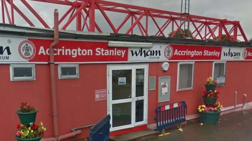 Accrington Stanley Football Club entrance. A one storey building in red and white with flowers in tubs