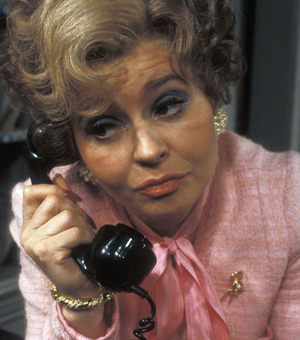 Prunella Scales in a pink top on the phone as Sybil in Fawlty Towers