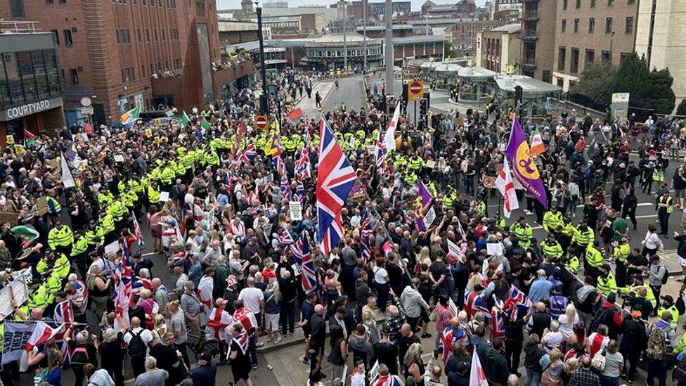 Crowds with flags attend the protest surrounded by police in high-vis jackets