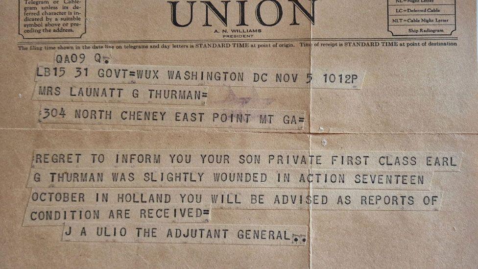 A close up of a Western Union telegram sent to Mrs Launatt G Thurman informing her her son has been slightly wounded in action. Its background is brown and the type written script is in upper case