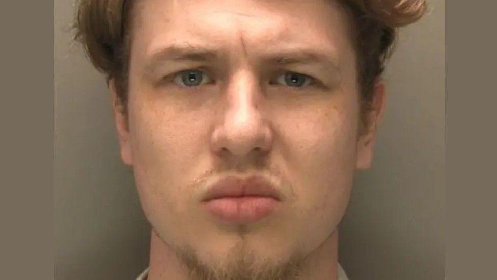 A police mugshot of Owen Blades. He has mousey-brown-blond hair and blue eyes, and is looking directly at the camera.