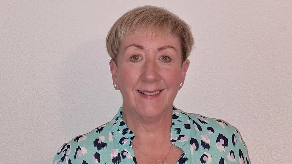 Heather Thompson. She has short blonde hair, wearing pearl earrings and a light green printed blouse. She is smiling at the camera.