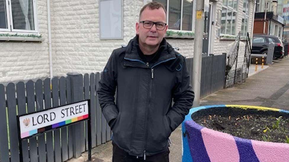 Shaun Pickup stands by the newly decorated Lord Street sign and a huge rainbow-painted street planter.