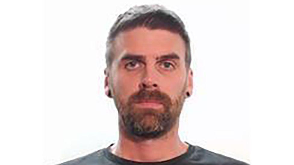 A police mugshot of Christopher Malcolm, a man with a beard looking at the camera.