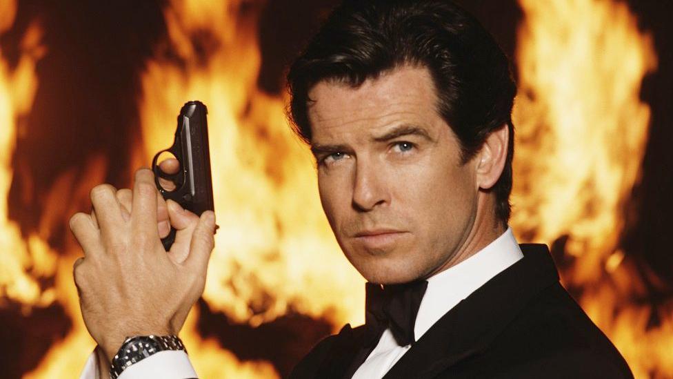 Pierce Brosnan as 007 in a tuxedo and bow tie, holding up a pistol.