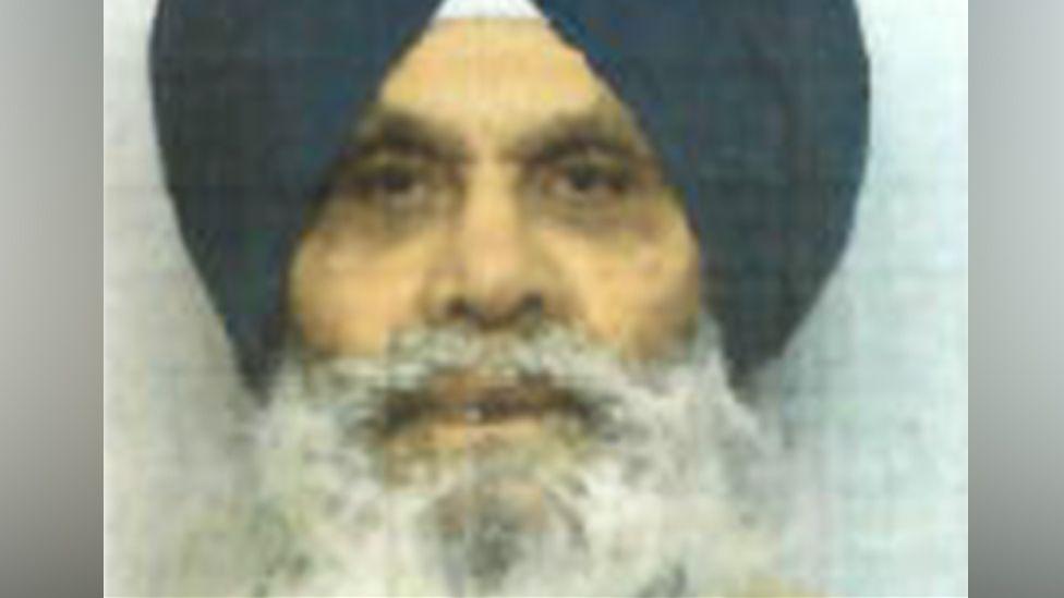 A blurry mugshot photo of Singh Mauji. He is wearing a black turban and has a bushy grey beard and moustache