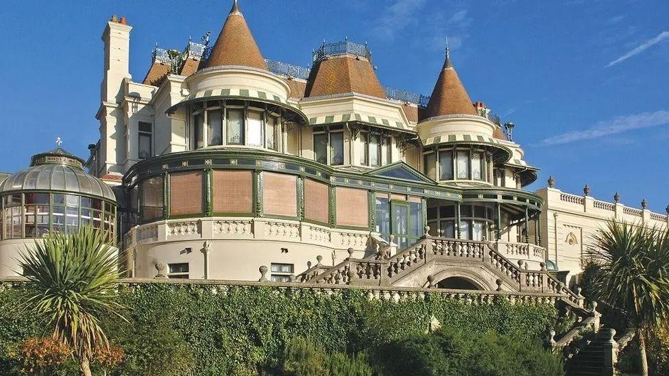 The Russell Cotes Museum - a Victorian building with turrets and external staircases set against a blue sky with palm trees in the foreground