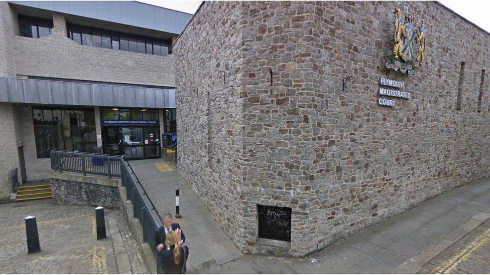 A photo which shows Plymouth Magistrates Court and Plymouth Youth Court. On the left is a building with windows and double doors. There is a ramp leading up to the doors on the right and stairs on the left. Next to the ramp is a brick building which has Plymouth Magistrates Court on the right of the building with a crest.