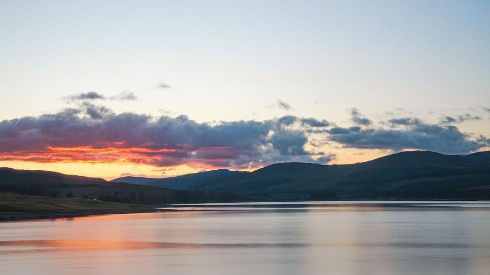 A sunset over a loch with rolling hills in the background