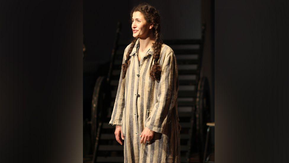 The actor playing Susan stands speaking to the audience, wearing a striped nightshirt.