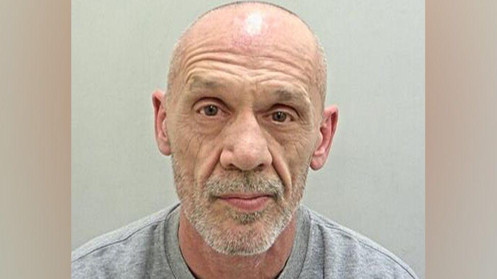 David Mitchell's police mugshot. He is bald, has white stubble and is wearing a grey sweatshirt