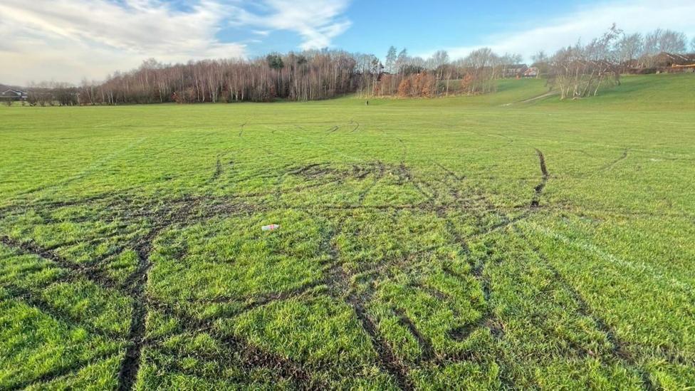 A playing field covered in muddy tracks caused by off-road bikes.