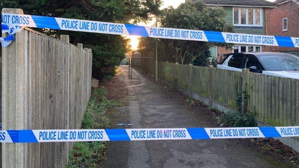 Path with railings in centre and police tape across a wooden fence runs along both sides