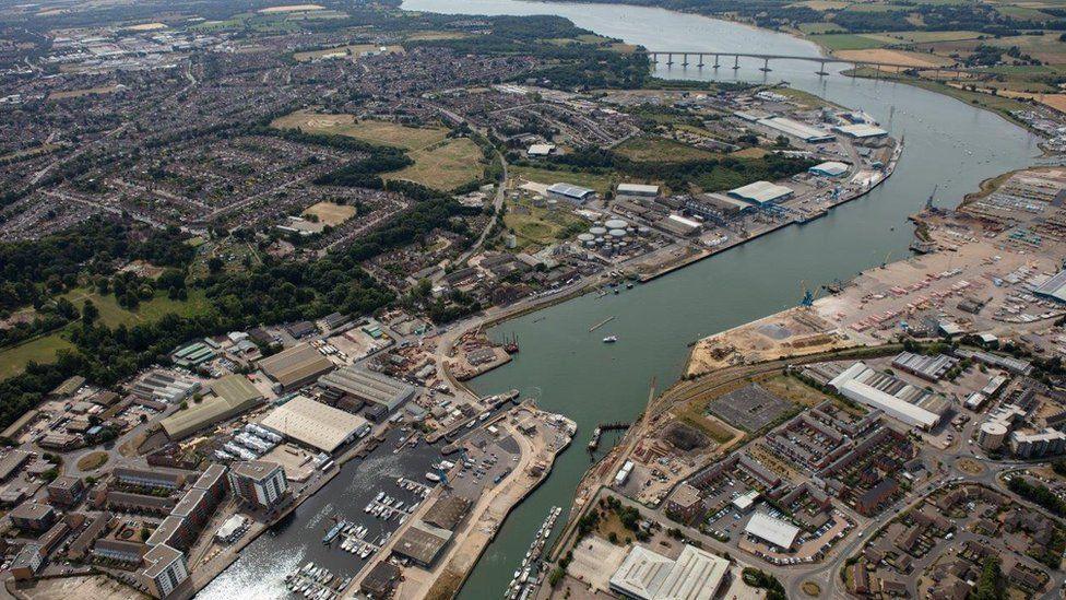 A drone image of Ipswich Port and Marina. A river can be seen winding through the land with boats moored in one area and various buildings lining the way. The Orwell Bridge that carries the A14 can be seen in the distance.