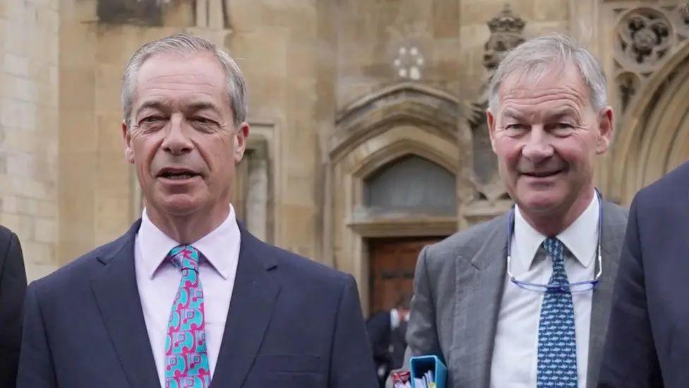 Nigel Farage, left, with Rupert Lowe outside Westminster. Farage is talking and Lowe is smiling. They are both wearing blue patterned ties and Lowe is holding some binders.