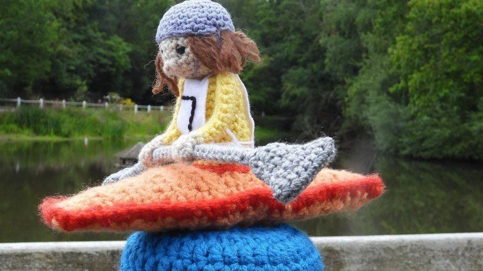 A woolly orange canoe on top of a post with a yellow-jersey wearing canoeist holding a grey oar with a black number 7 on their race bib