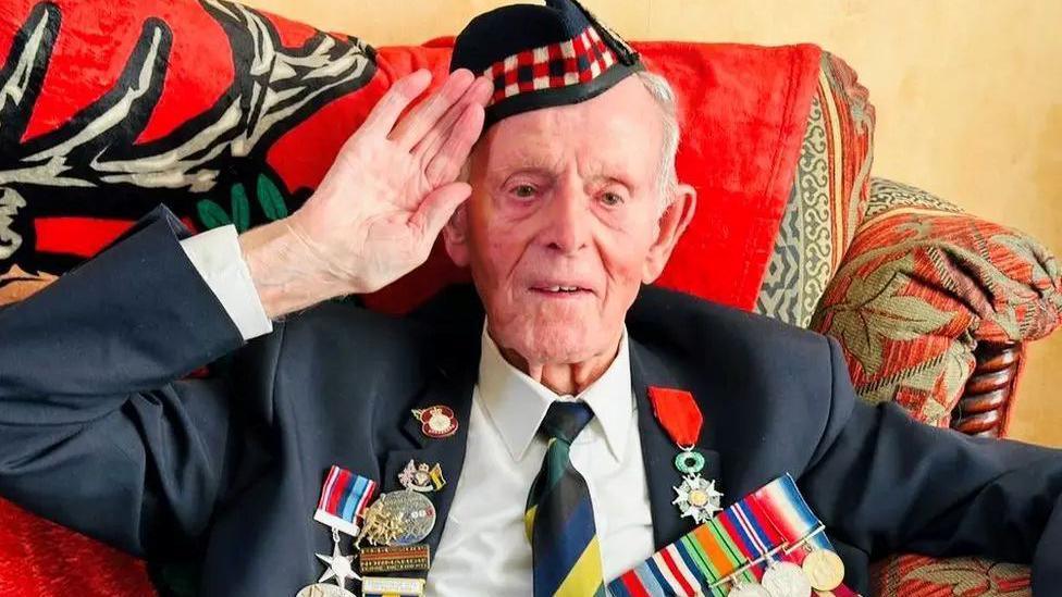 Veteran Jim Glennie in uniform with medals, smiling and saluting.
