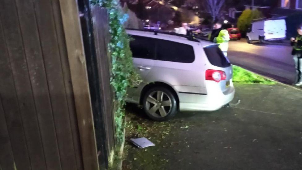 The profile of the back end of a VW Passat which has crashed through a hedge