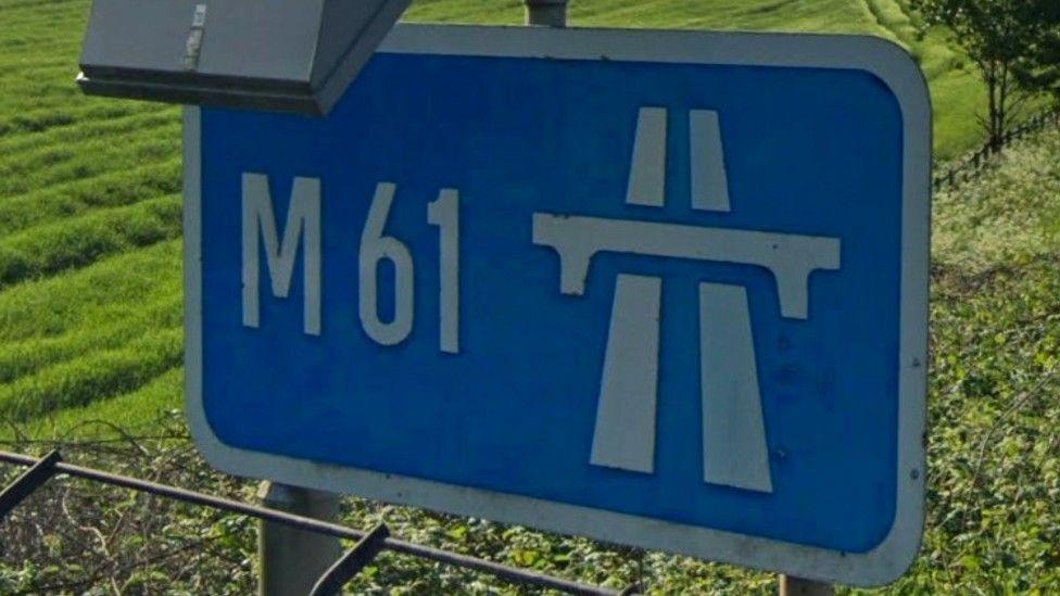 A screenshot of a blue road sign which says "M61" in white writing. 