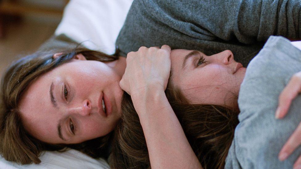 Two young women, one embracing the other