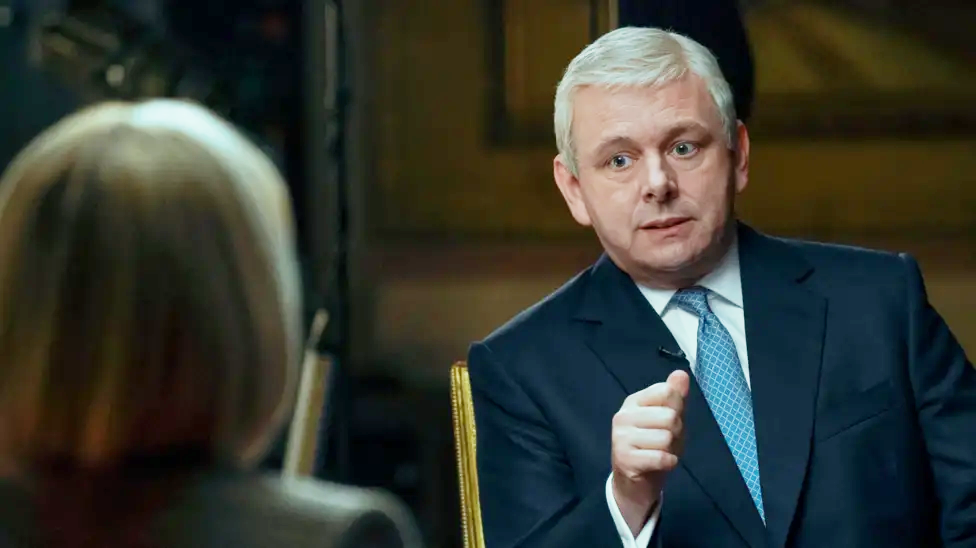 Michael Sheen in a blue suit and tie, and white shirt, as Prince Andrew in A Very Royal Scandal, being interviewed by the actor playing Emily Maitlis