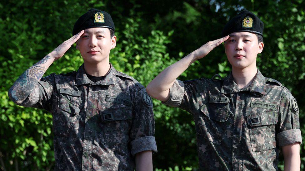 BTS members Jungkook and Jimin in military uniforms giving a salute