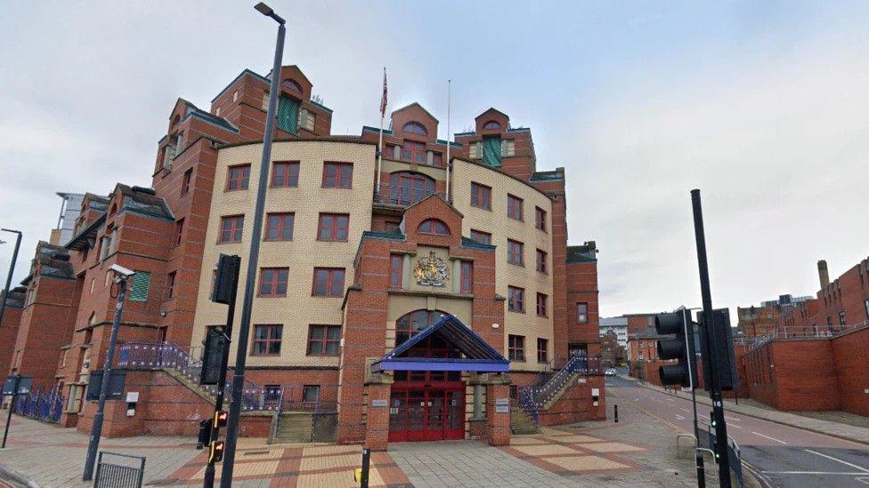 The outside of Leeds Magistrates' Court: a large red-brick building. Lamp-posts and other street furniture can be seen.