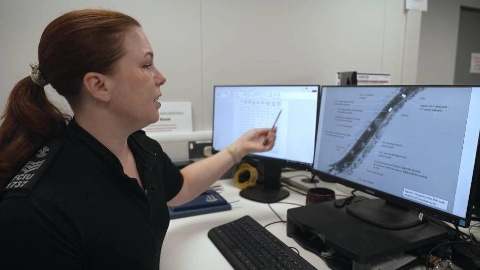 A person with reddish hair tied in a pontytail is seen at a computer with two screens