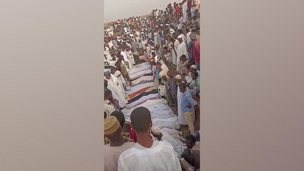 Bodies wrapped in cloth surrounded by a large group of mourners.