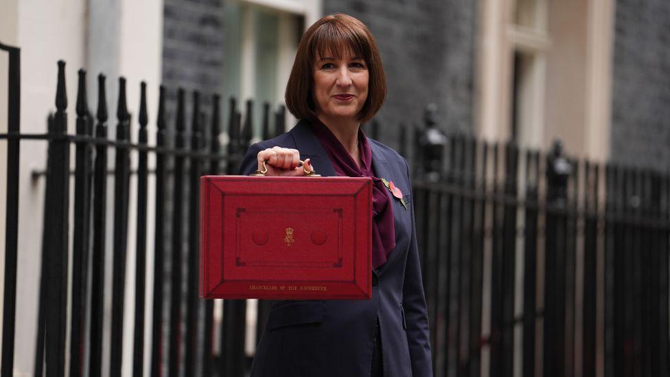 The chancellor, wearing a dark suit, holds up a red box outside Downing Street 