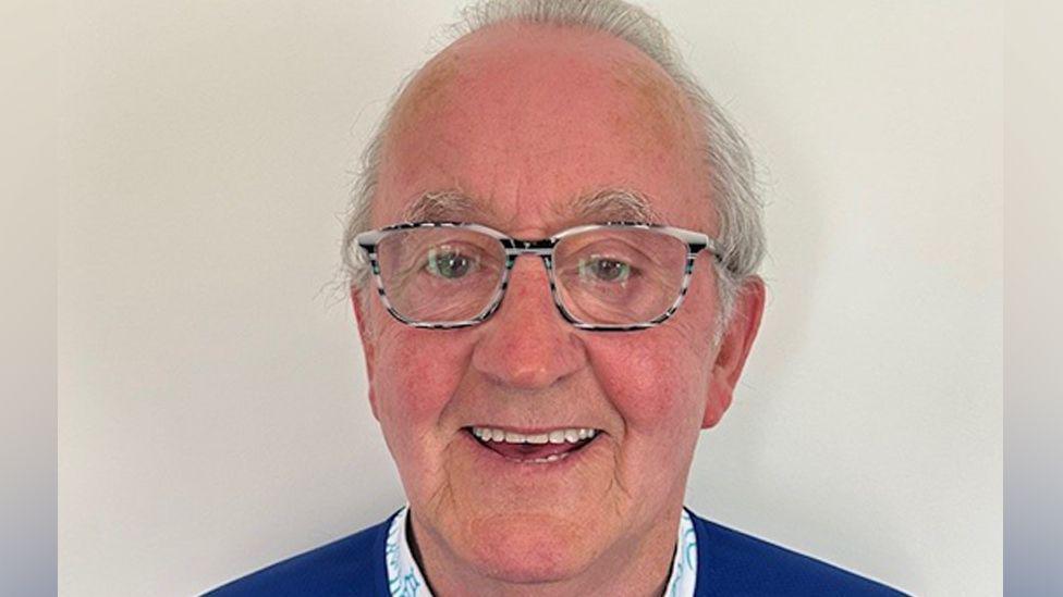 A head and shoulders picture of John Gerard Boyle who is smiling at the camera in front of a white wall.