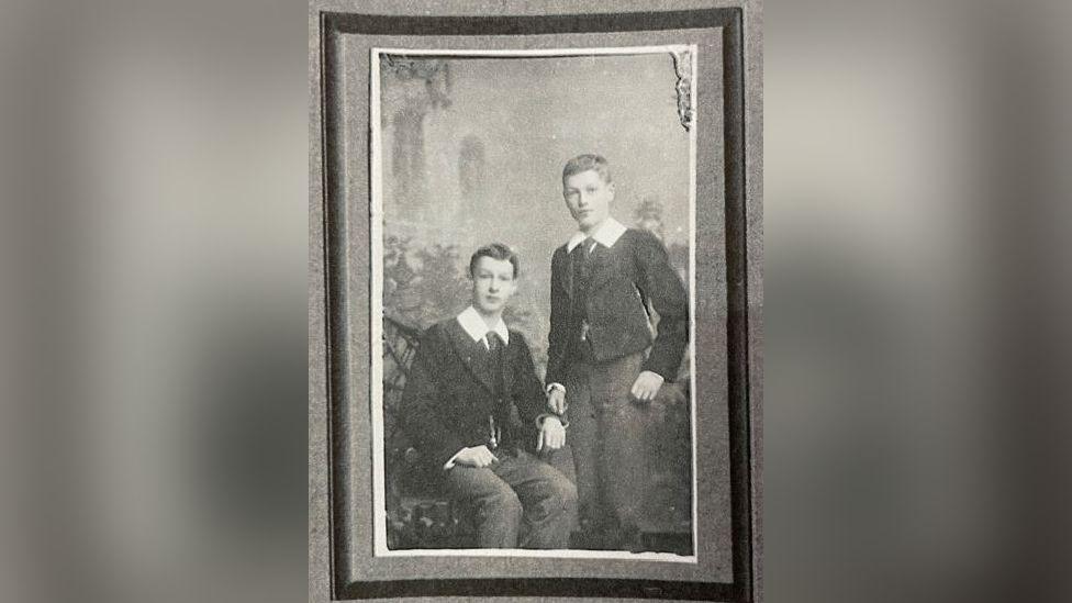 An old photo of Ewart and Stanley. Two boys dressed in smart black jackets with a thick white collar. The photo is black and white. 