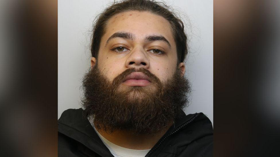 A mugshot of Jardel Edwards - he is wearing a white T-shirt and black hoodie and has a beard and brown hair.