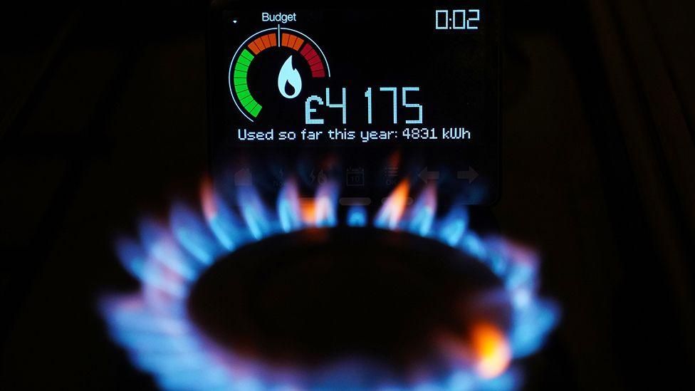 A gas ring on a cooker hob with a smart meter in the background