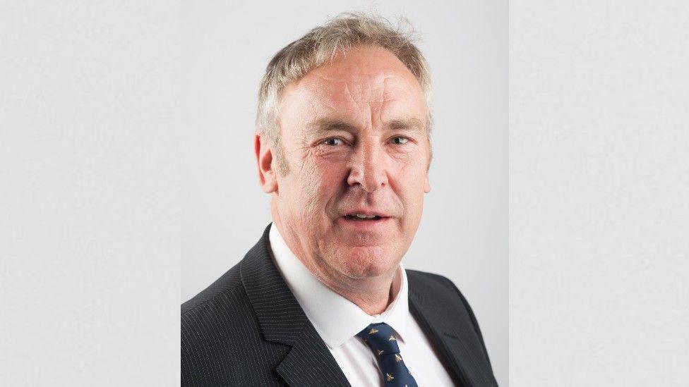 Headshot of councillor Vernon Smith who is wearing a dark blazer and tie and has short light brown/grey hair