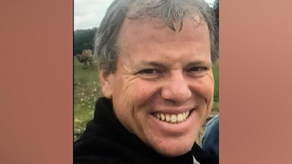 Donald McPherson, who is wearing a black turtleneck jumper, smiles while stood outside.