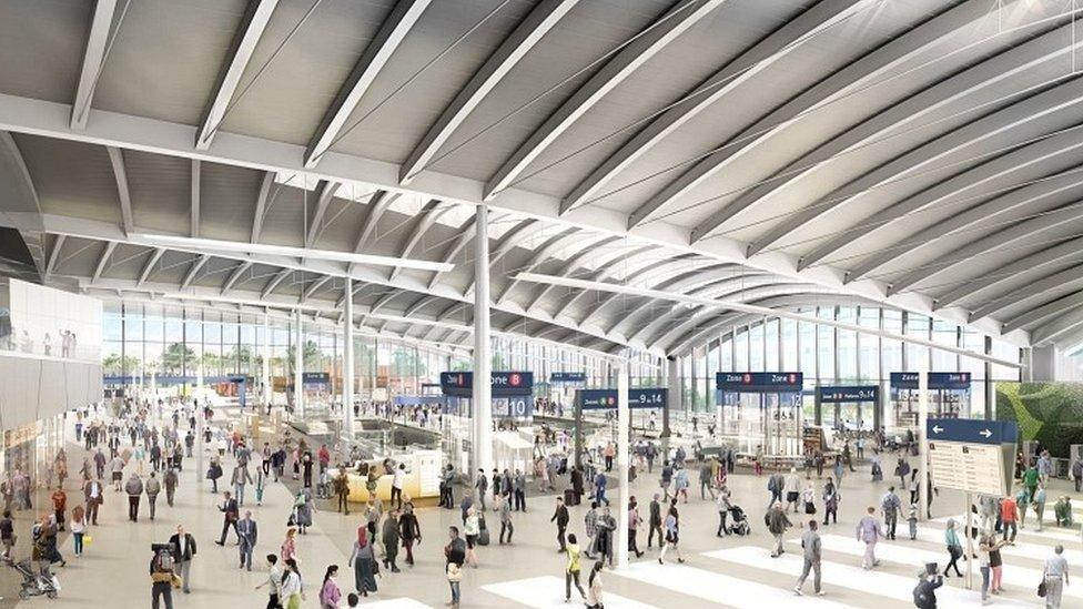 A computer generated image of what the new station at HS2 will look like. It is a large white station with a very high metal panelled ceiling and walls made of glass. There are lots of people walking around with bags, a large pedestrian crossing and information boards dotted around.