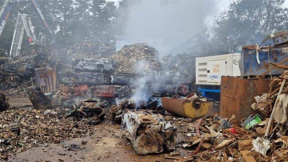 Piles of scrap metal and heaps of fragments on the ground crushed vehicles in cube shapes with smoke rising