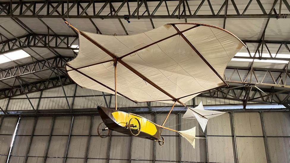 A replica of  glider with a canoe-like object for sitting in and a large piece of cream coloured material above