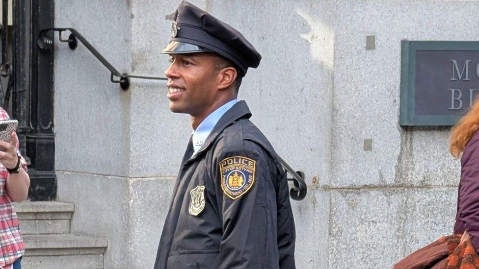 An actor on set dressed in a City of Gotham Police uniform