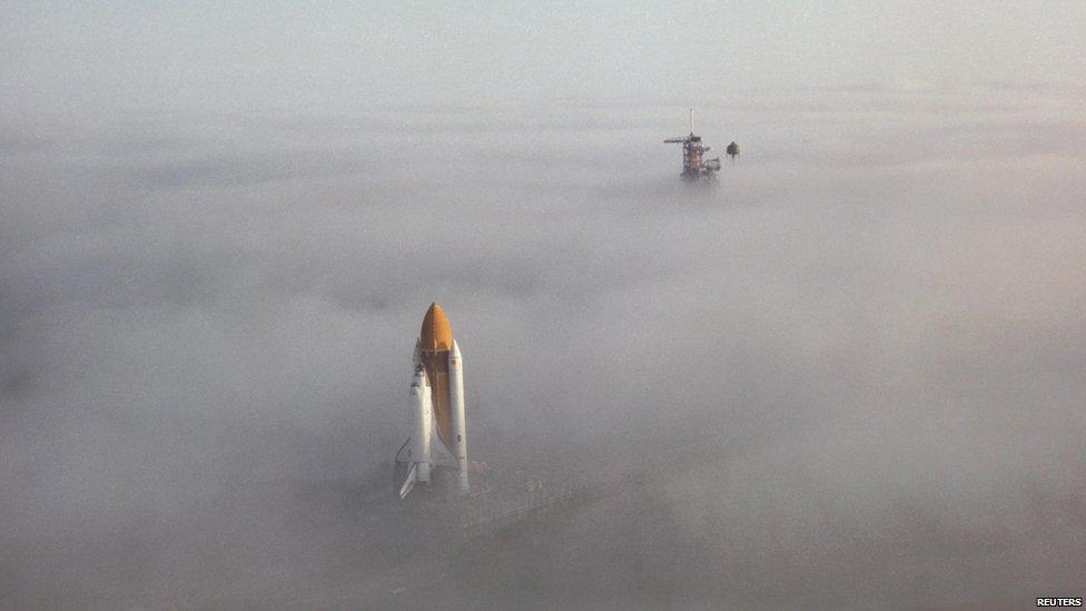 Space shuttle Challenger moving through fog to launch pad.