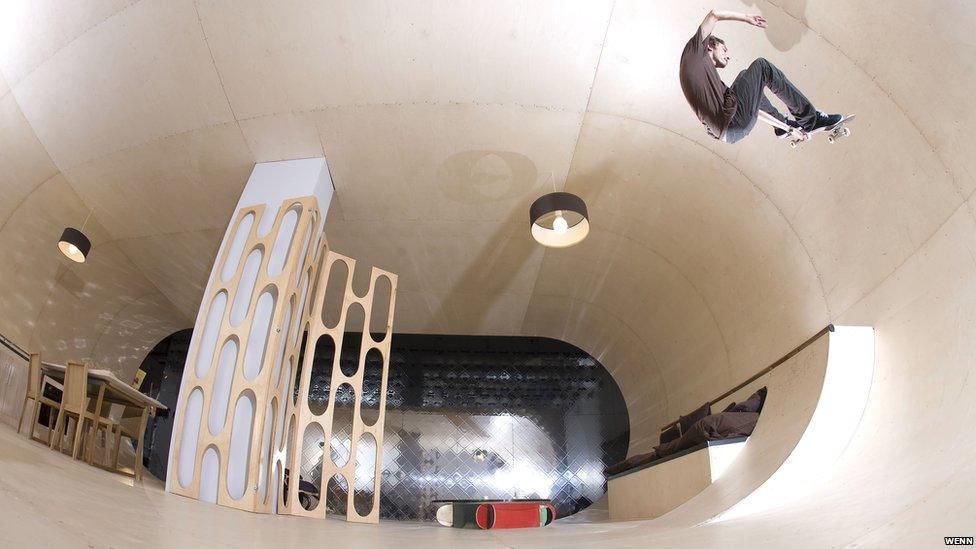 Skateboarder skating up the wall of the house.