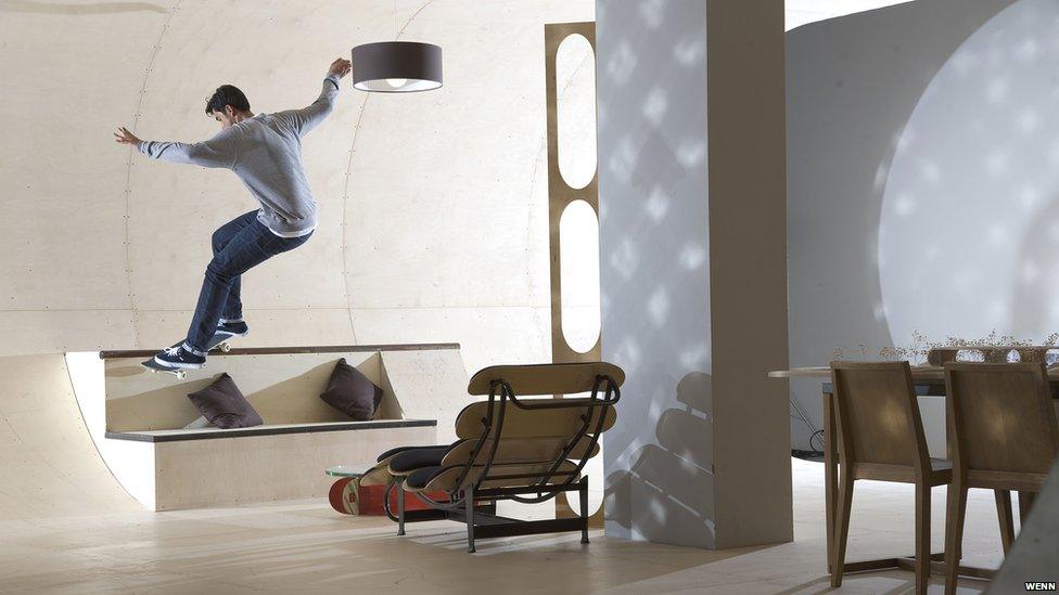Skateboarder skating along the wall of the house.