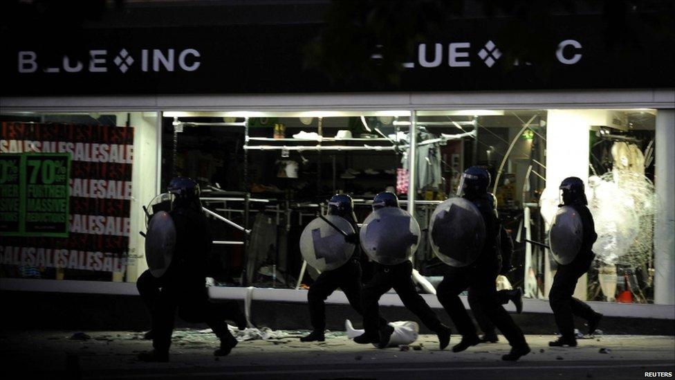 Police in full riot gear run down a shopping street in Peckham, London