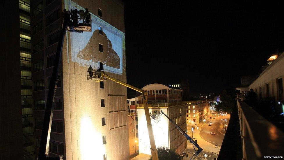 Graffiti artists in cranes being lifted to reach the tops of high rise buildings in Bristol.