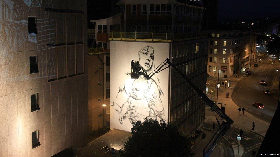 Two graffiti artists look at their painting of a mother holding a baby in Bristol.